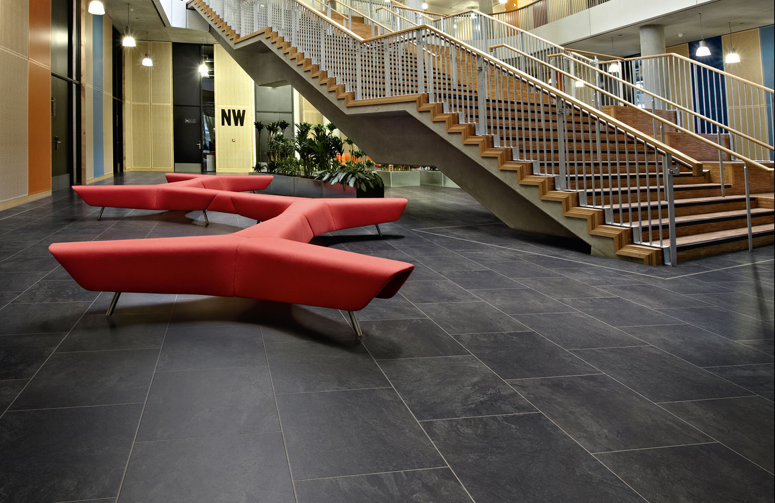 a spacious room with black stone tiles, a staircase and a large red chair