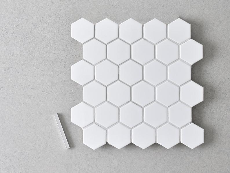 Mapei groute and white hexagonal mosaic tiles on a grey concrete background