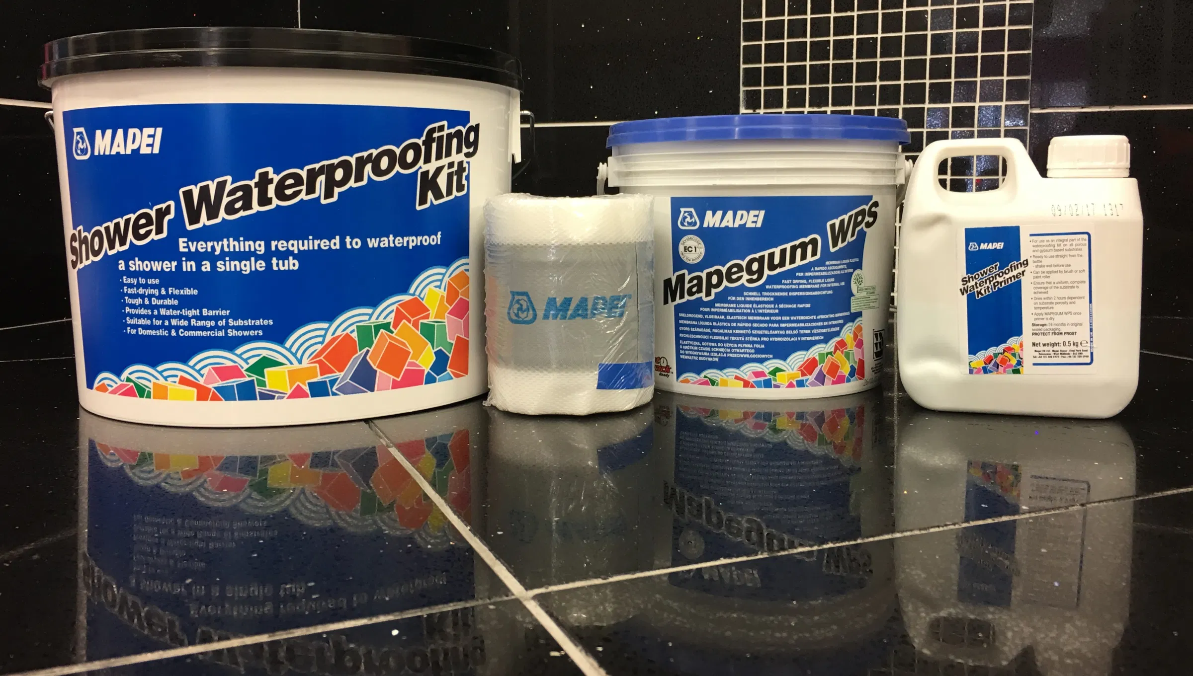 a bathroom with shiny black tiles and white and blue tubs of mapegum waterproofing equiptment